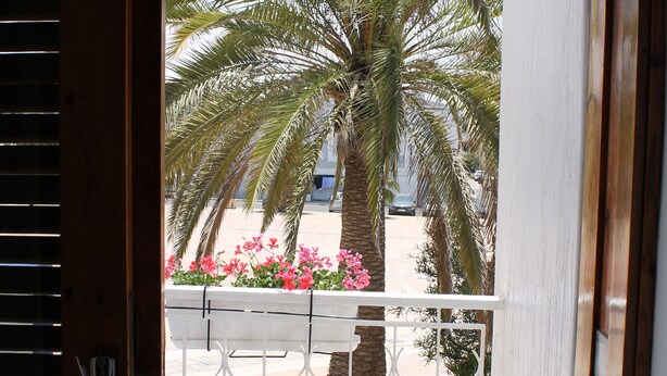 A wooden door with a view of a balcony, a palm tree, and a chair. - Hotel Sindibad (Agadir)