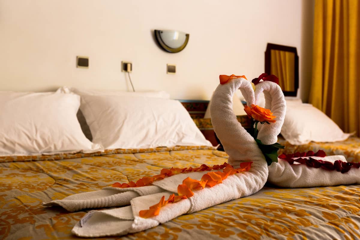 Una cama bien hecha con una colcha estampada con motivos florales y una escultura de toallas con forma de cisnes y flores naranjas.