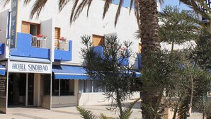A hotel named 'Hotel Sindbad' with a blue awning, a palm tree, and a tiled planter with small plants. - Hotel Sindibad (Agadir)