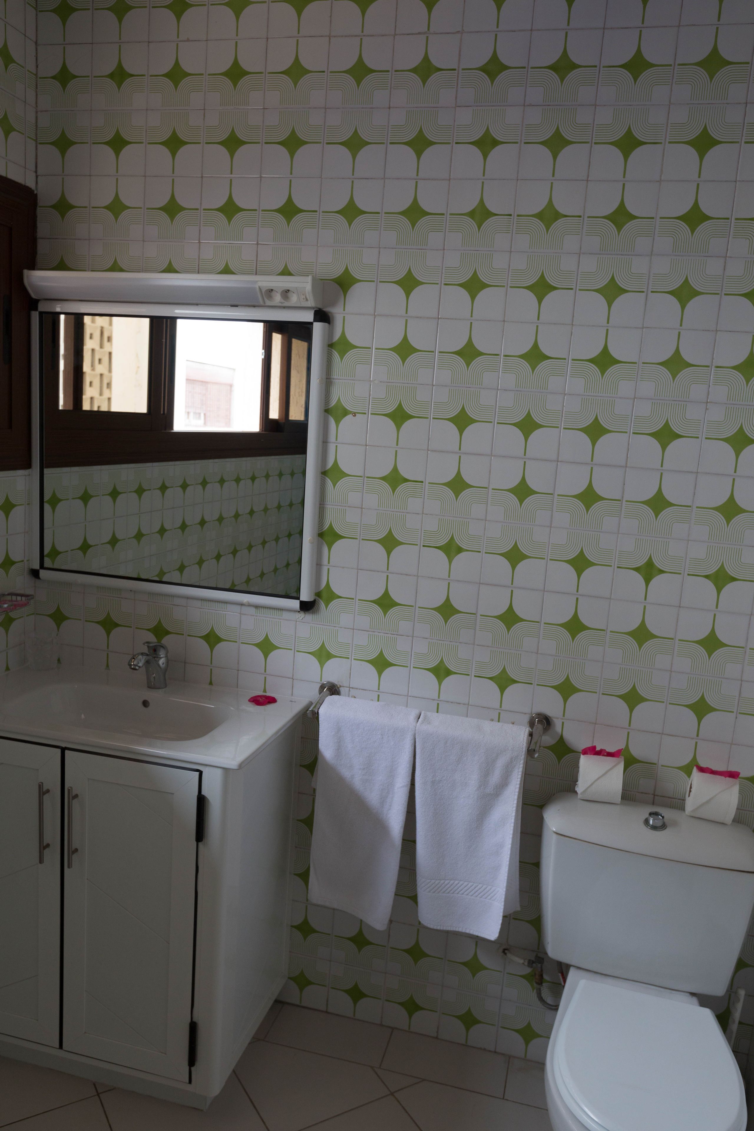 Un baño con un lavabo blanco, espejo y retrete. Hay dos toallas blancas colgadas en la pared.