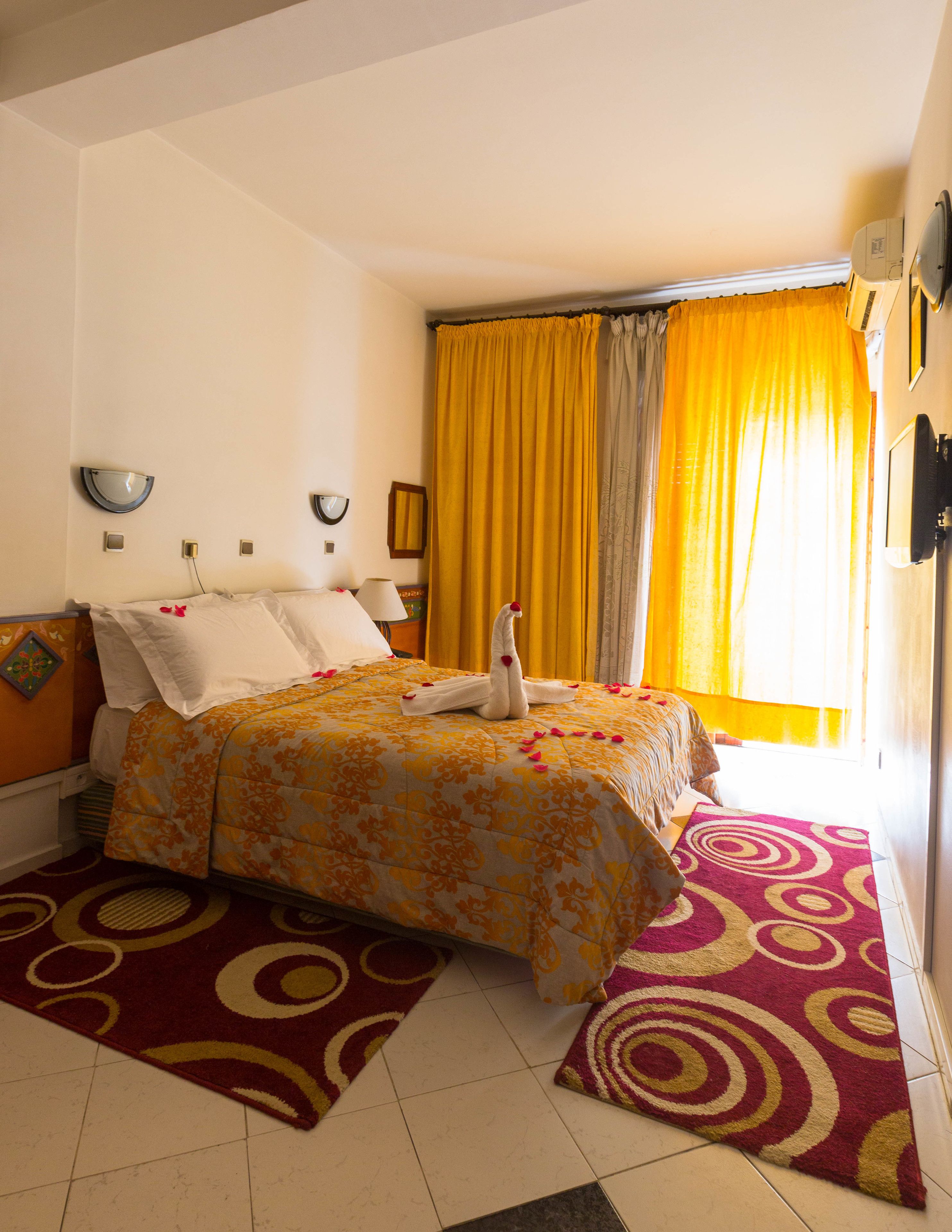 Habitación de hotel con cama, un ventanal con cortinas amarillas, aire acondicionado de pared y aplique.