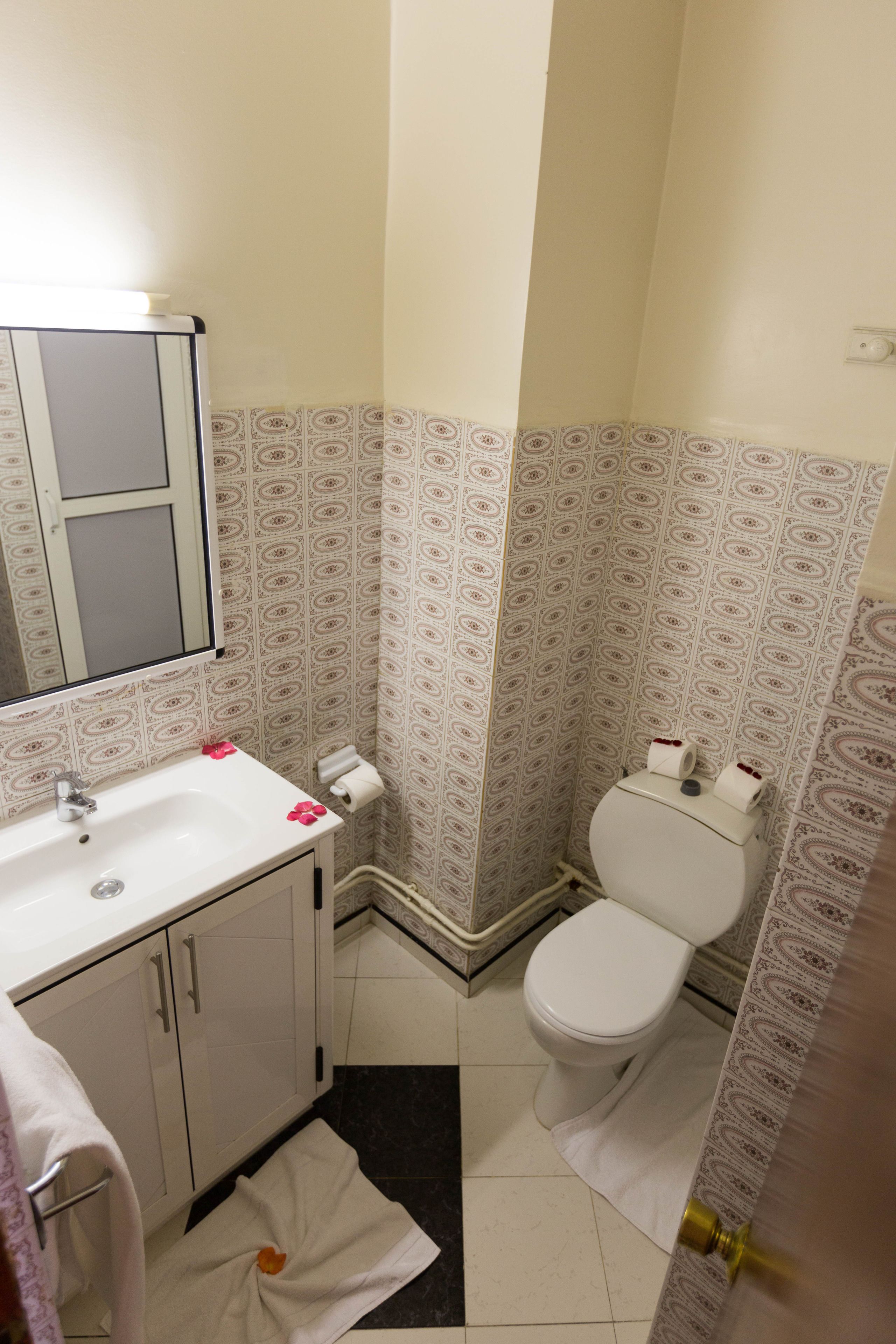 A bathroom with a white sink, mirror, and toilet. There are patterned tiles on the walls and floor.