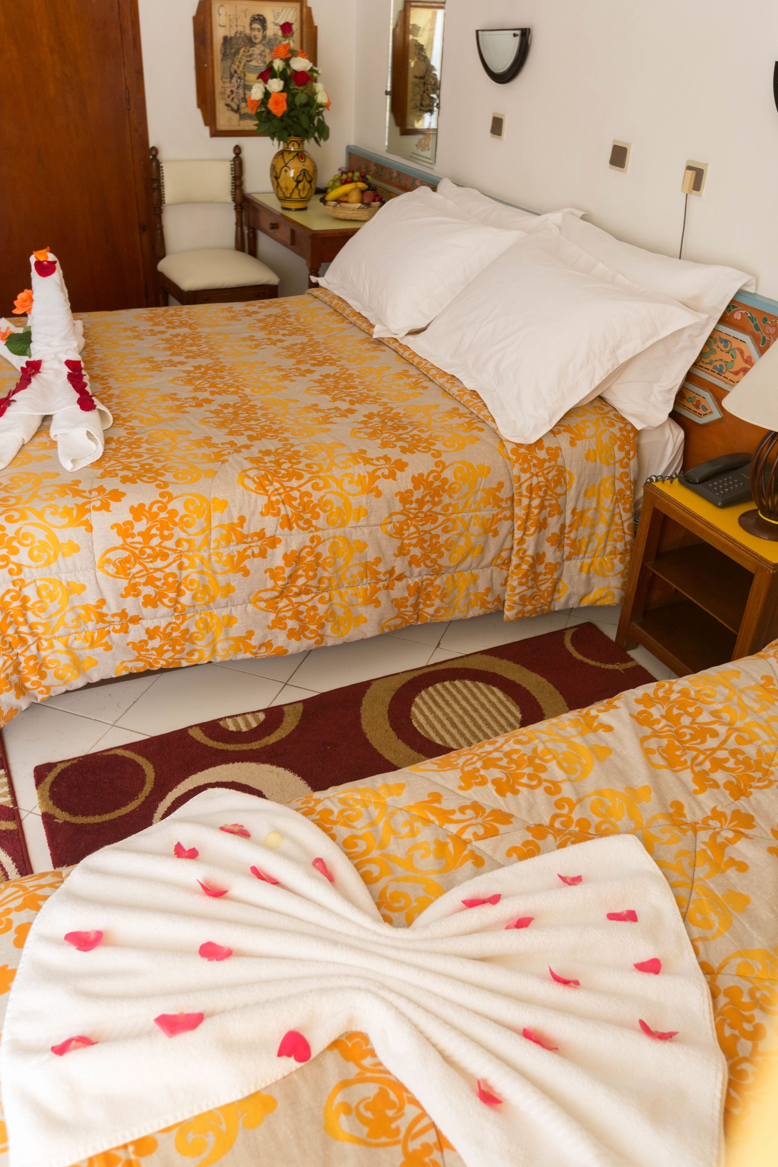 Une chambre d’hôtel avec deux lits, une table de chevet en bois, une chaise, un vase avec des fleurs, un tableau encadré au mur et un téléphone sur la table de chevet.