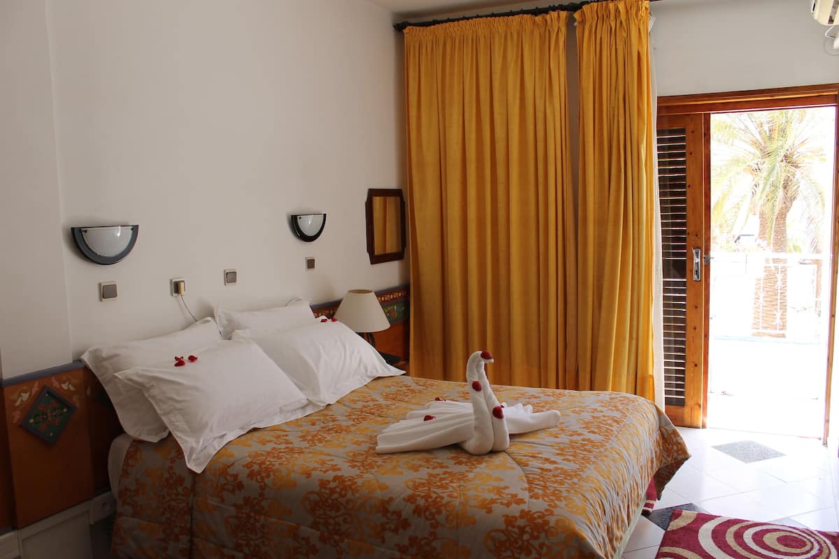 Habitación de hotel con una cama, una lámpara de pared, un espejo y un ventanal con cortinas.