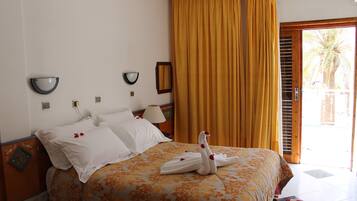 A hotel room with a bed, a wall-mounted lamp, a mirror, and a window with curtains.