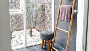 A bathroom with a glass door leading to a garden, a wooden ladder with towels, and a small stool. - Dejavu Hotel (Gili Trawangan)