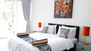 A bedroom with a bed, two bedside tables, a nightstand, a window with curtains, and a painting on the wall. - Dejavu Hotel (Gili Trawangan)