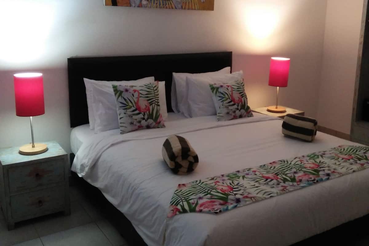 Ein Schlafzimmer mit einem Bett, zwei Nachttischen, einer Lampe auf jedem Tisch, einem Kissen mit Blumenmuster und einem Bild an der Wand.