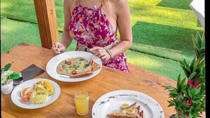 A person seated at an outdoor wooden table with a plate of food, a glass of juice, and a potted plant. - Dejavu Hotel (Gili Trawangan)