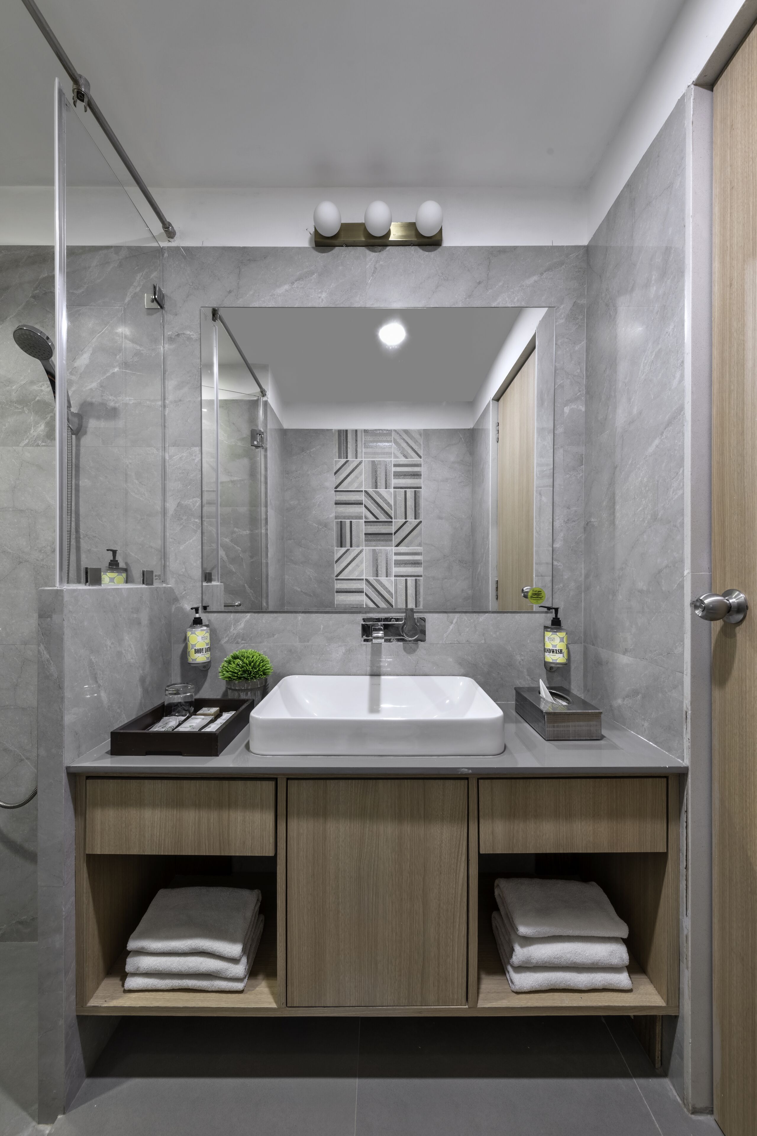 A modern bathroom with a large mirror, a sink, and a shower. There are towels and toiletries on the counter.