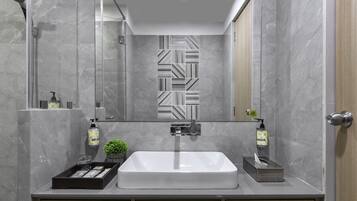 A modern bathroom with a large mirror, a sink, and a shower. There are towels and toiletries on the counter.