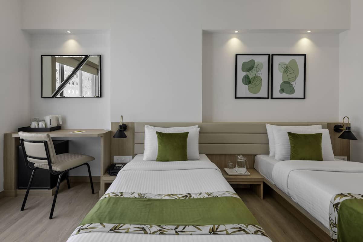 A hotel room with two beds, a desk, and a chair. There are framed pictures on the wall and a mirror above the desk.