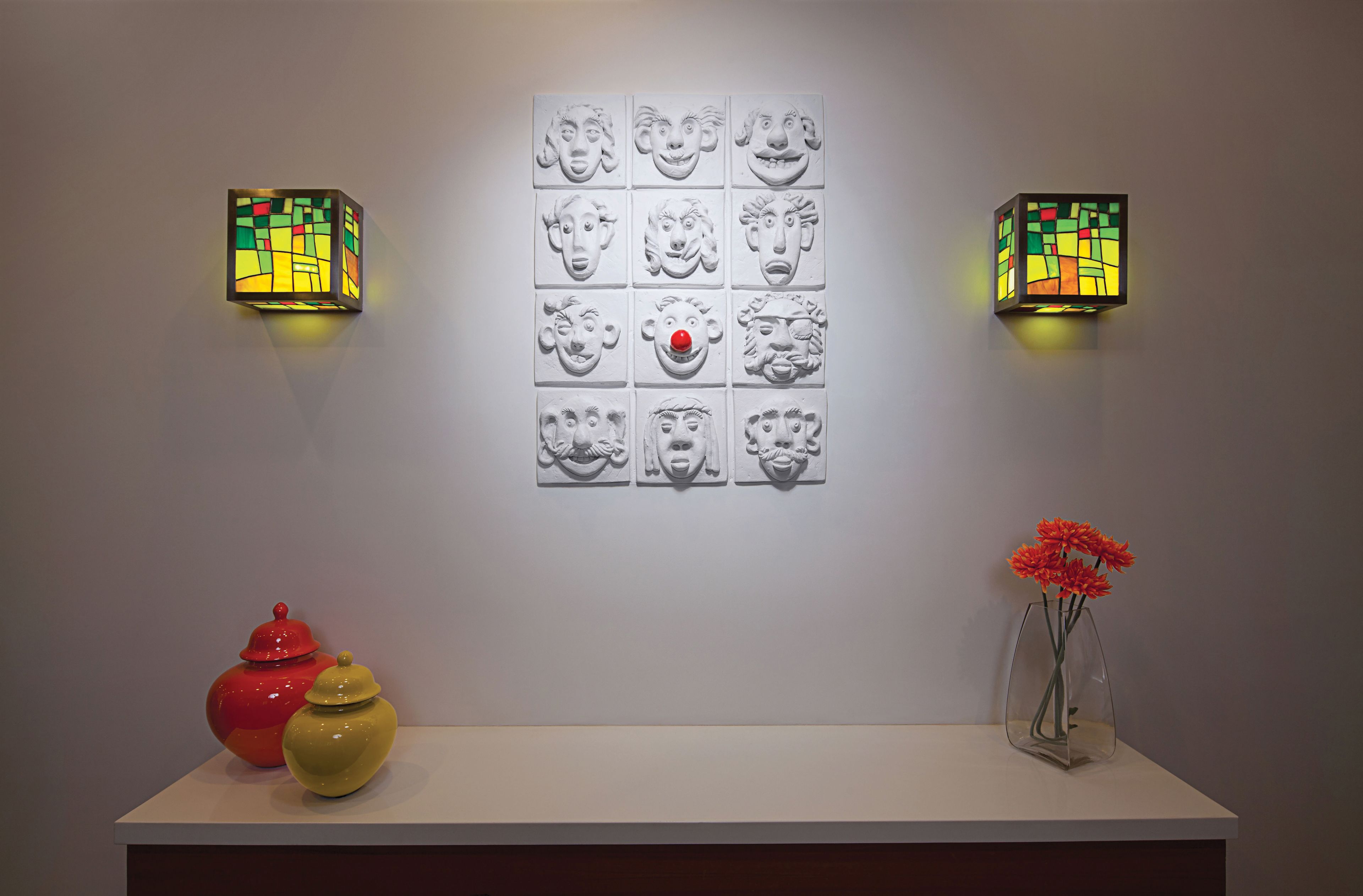 A wall with a grid of 12 head sculptures and two wall-mounted light fixtures.