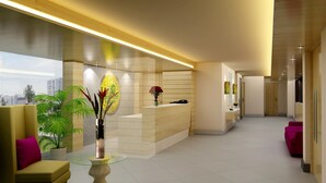 A modern reception area with a reception desk, a vase with flowers, a plant, and a city view through large windows. - Lemon Tree Hotel Vadodra (Vadodara)