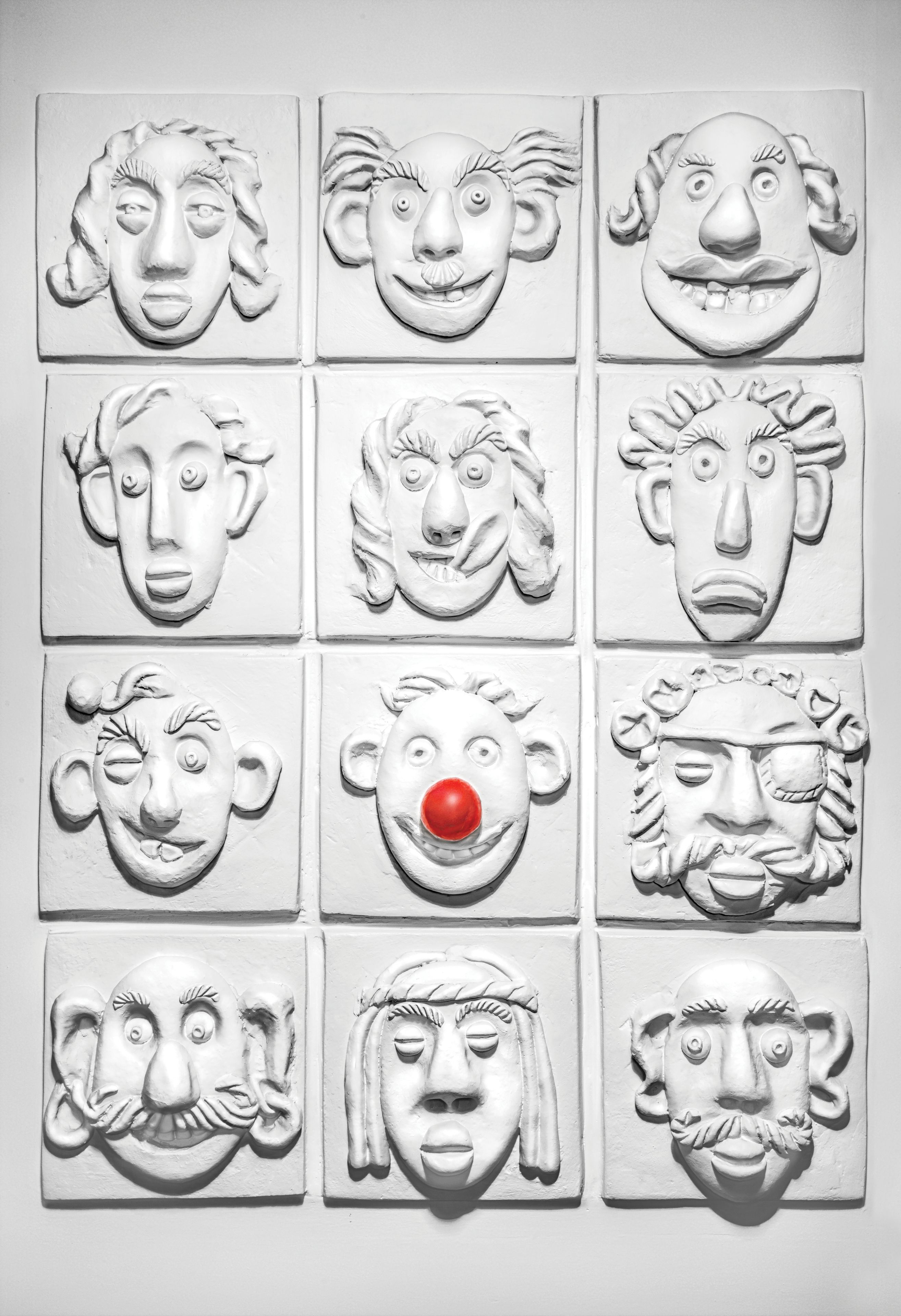 A wall with twelve white, textured panels, each depicting a different face.