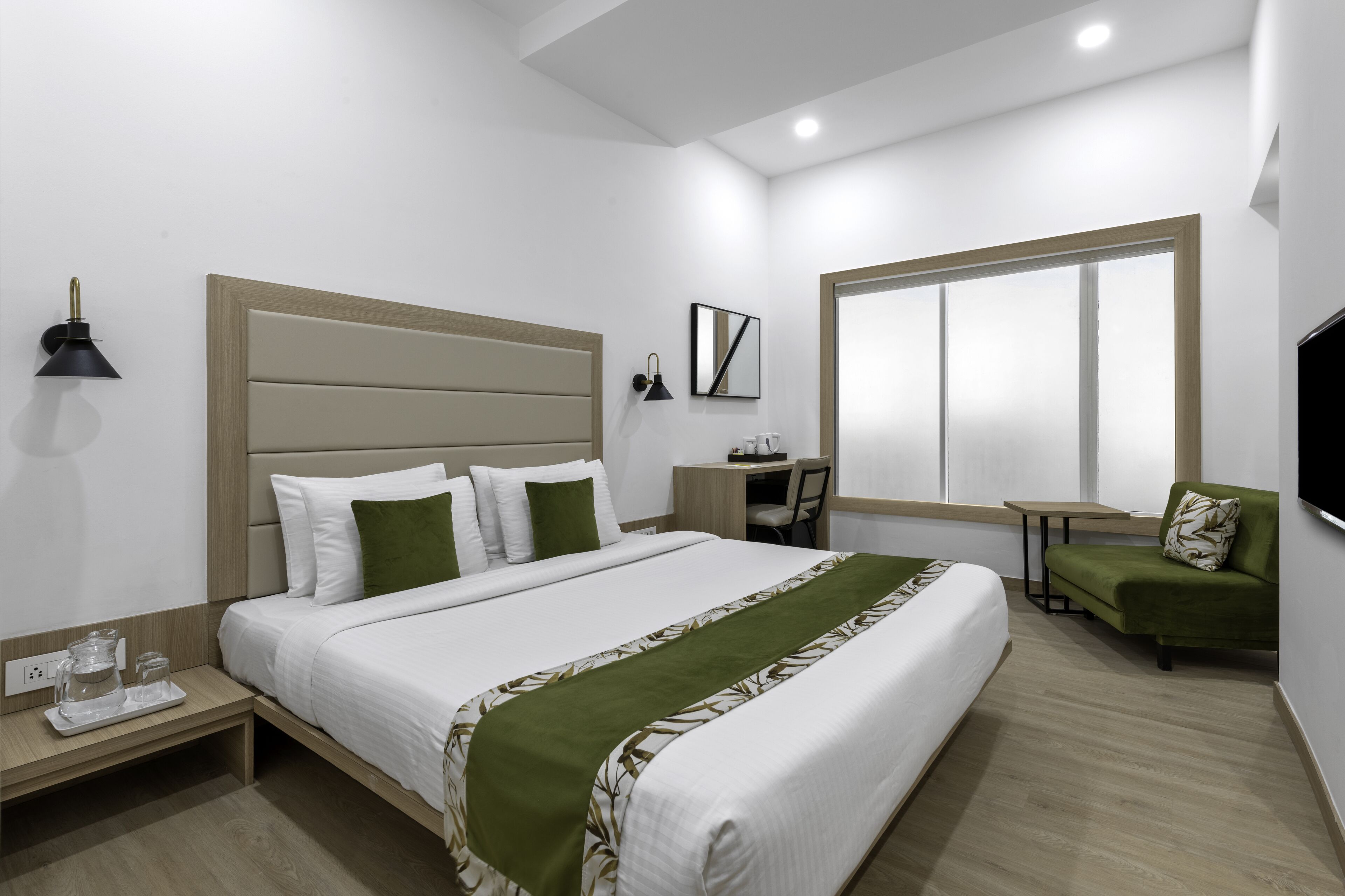 A modern hotel room with a large bed, a desk, a chair, and a TV.