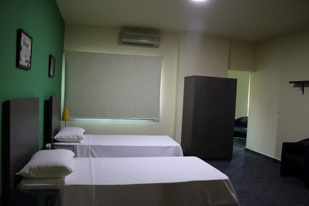 A hotel room with two beds, a wardrobe, a desk, and a window with a blind.