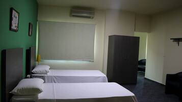 A hotel room with two beds, a wardrobe, a desk, and a window with a blind.