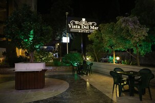 An outdoor seating area with a sign for Vista Del Mar Hotel, surrounded by trees and greenery.