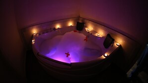 Un jacuzzi con chorros de agua, rodeado de velas, en una habitación con poca luz.