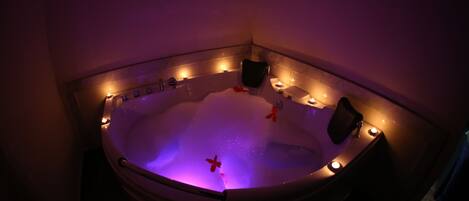 Un jacuzzi con chorros de agua, rodeado de velas, en una habitación con poca luz.