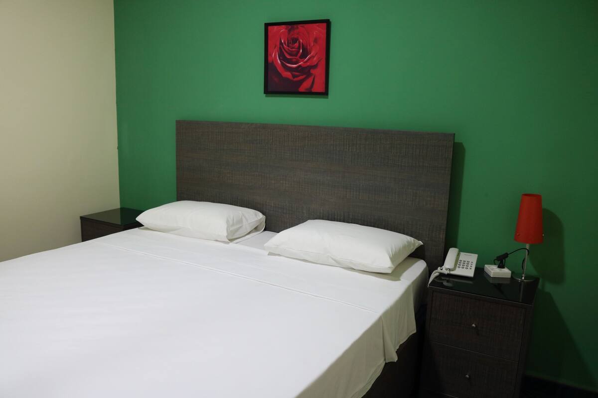 A neatly made bed with white linens, a grey headboard, and a red telephone on a bedside table.