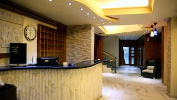 A hotel reception area with a marble counter, a clock, and a staircase leading to the dining area.