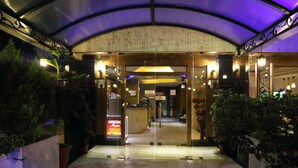 Entrada de hotel con puerta de vidrio, plantas en macetas y un cartel de Nescafé.