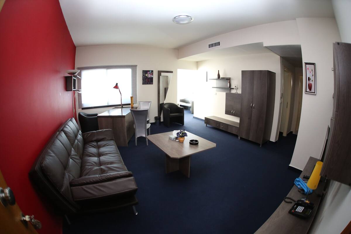 A compact living space with a sofa, a coffee table, a dining table, and a kitchen area.
