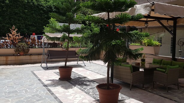 Un patio al aire libre con plantas en macetas, mobiliario de mimbre y piso de baldosas.