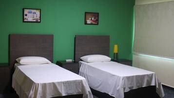 Dos camas individuales con cabeceras, una pared verde, una alfombra estampada y una ventana con persianas.