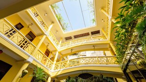 Un atrio de varios niveles con paredes amarillas y balcones, con tragaluces y plantas de interior.