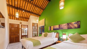 Habitación de hotel con dos camas, vigas de madera en el techo, una pared verde y un cuadro sobre las camas.