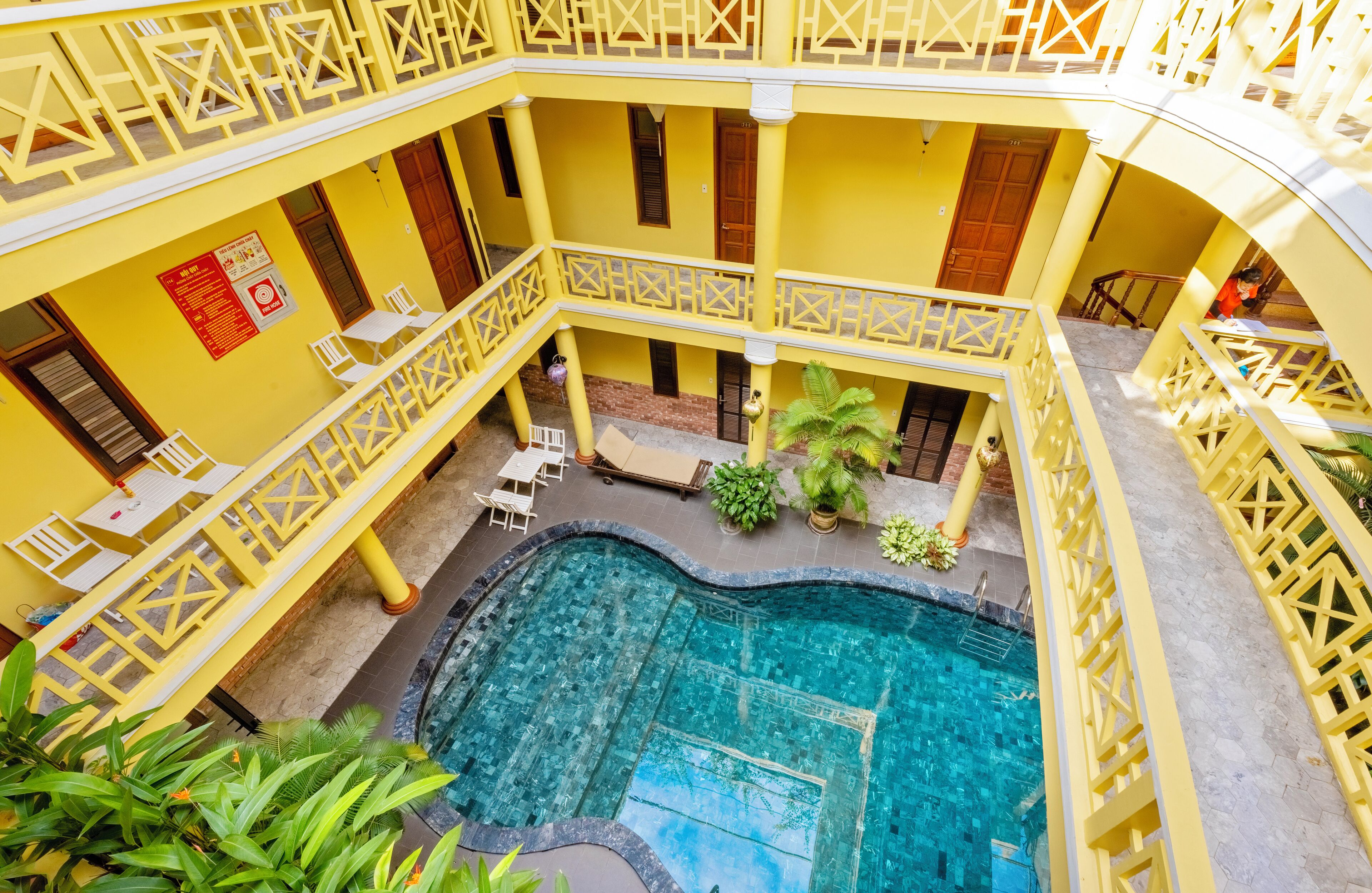 A multi-level yellow building with a central swimming pool, outdoor seating, and potted plants.