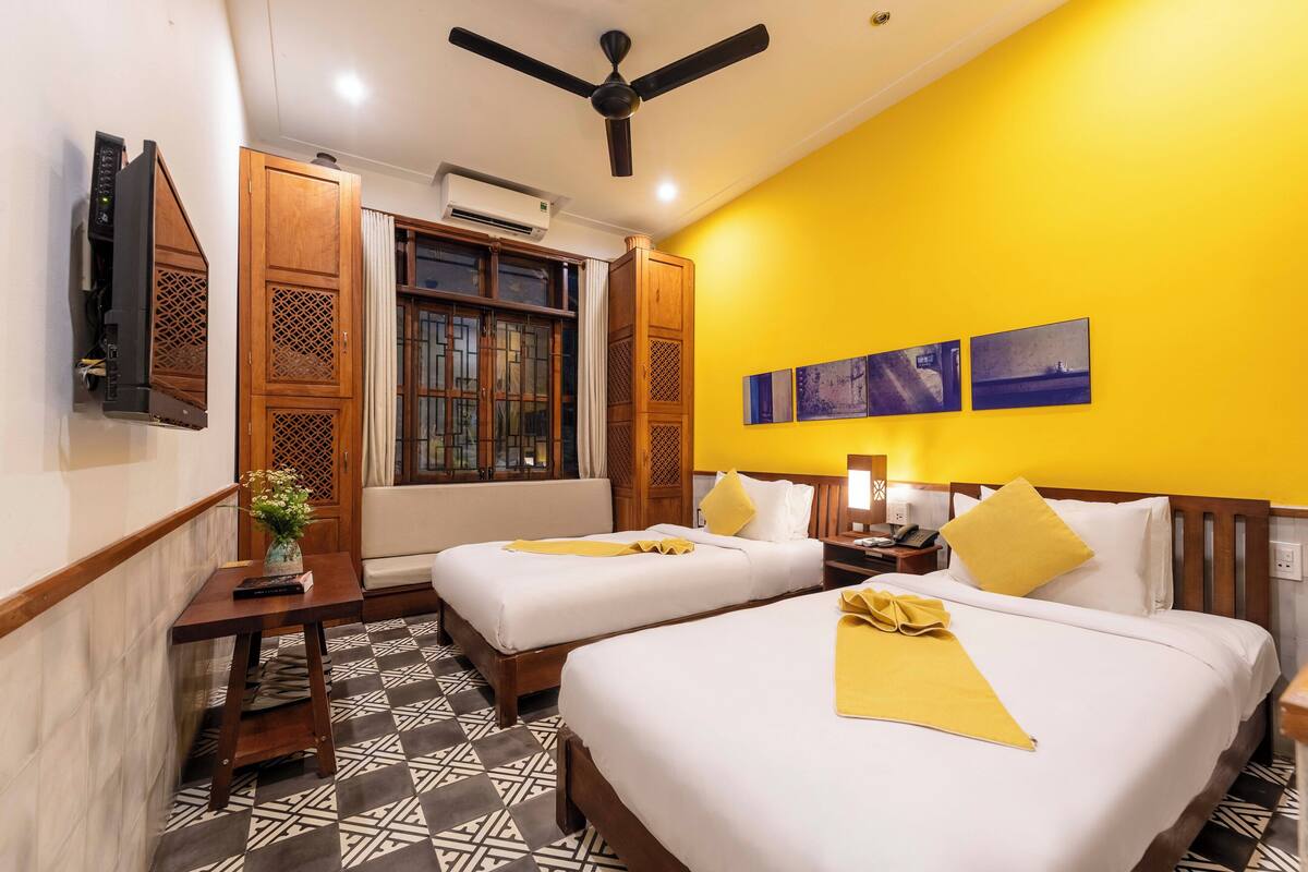 A hotel room with two beds, a ceiling fan, a TV, and a window with curtains.