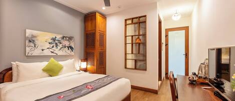 A hotel room with a bed, wooden wardrobe, a dining table, and a television.