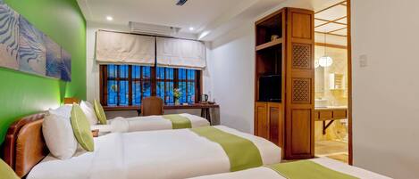A hotel room with two beds, a desk, a chair, a ceiling fan, and a view of the outside through a window.