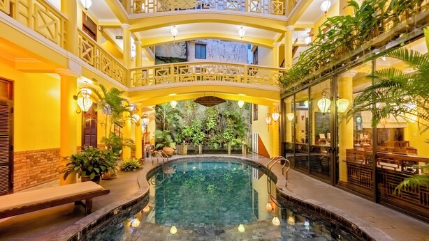 Una piscina interior con cerramiento de vidrio, rodeada de paredes amarillas y barandillas de madera.