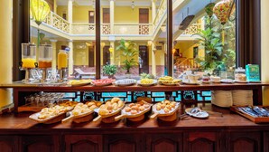 Un bufé con diversas opciones de comida y bebidas, un balcón con vista al patio interior, y un estilo arquitectónico tradicional con balcones y barandillas.