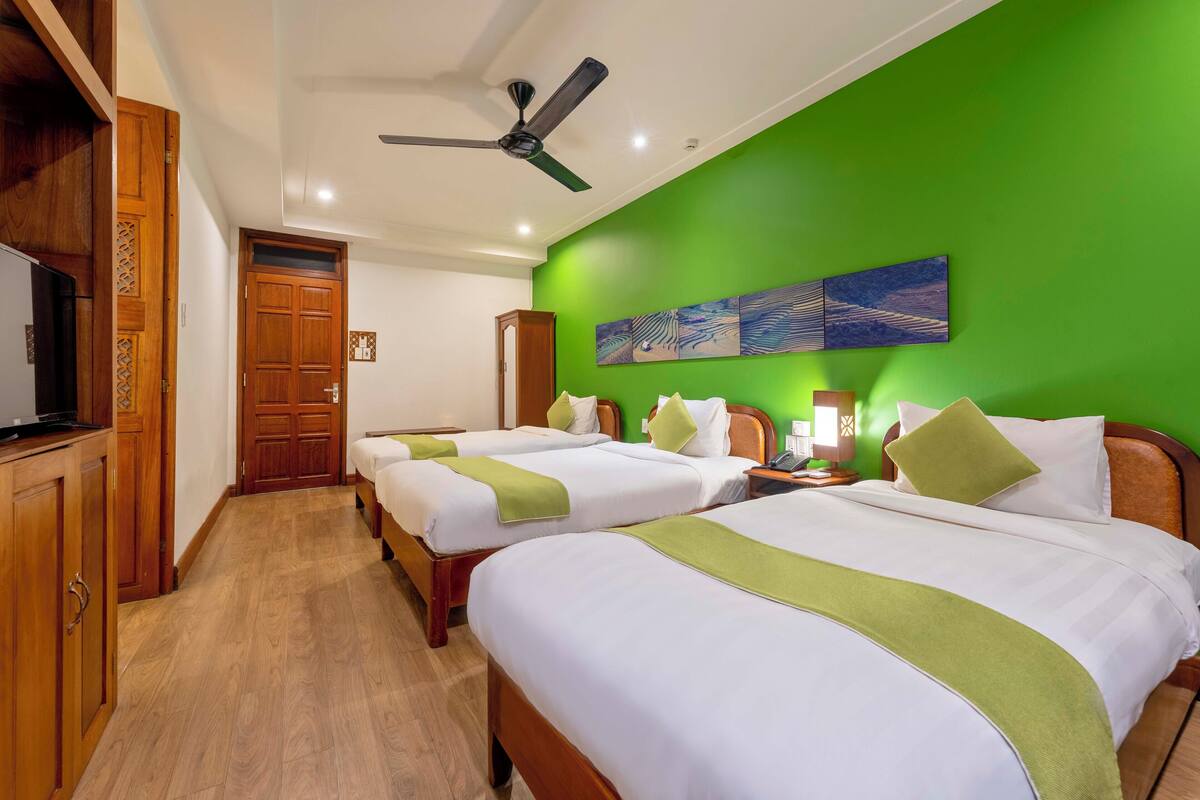 A hotel room with two beds, wooden furniture, a ceiling fan, and a green wall.