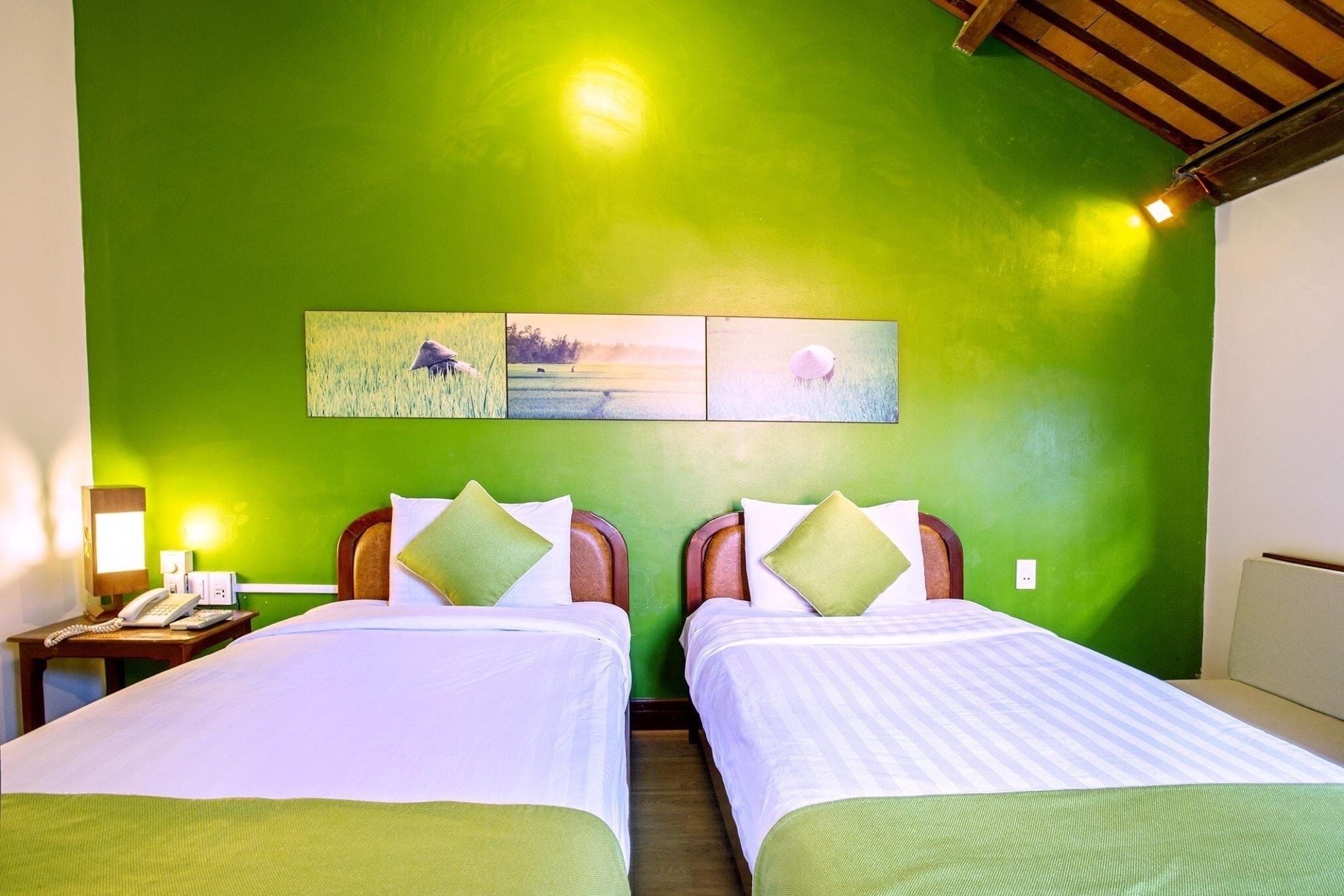 A room with two beds, green walls, and a wooden ceiling. There are two bedside tables with lamps and a phone.