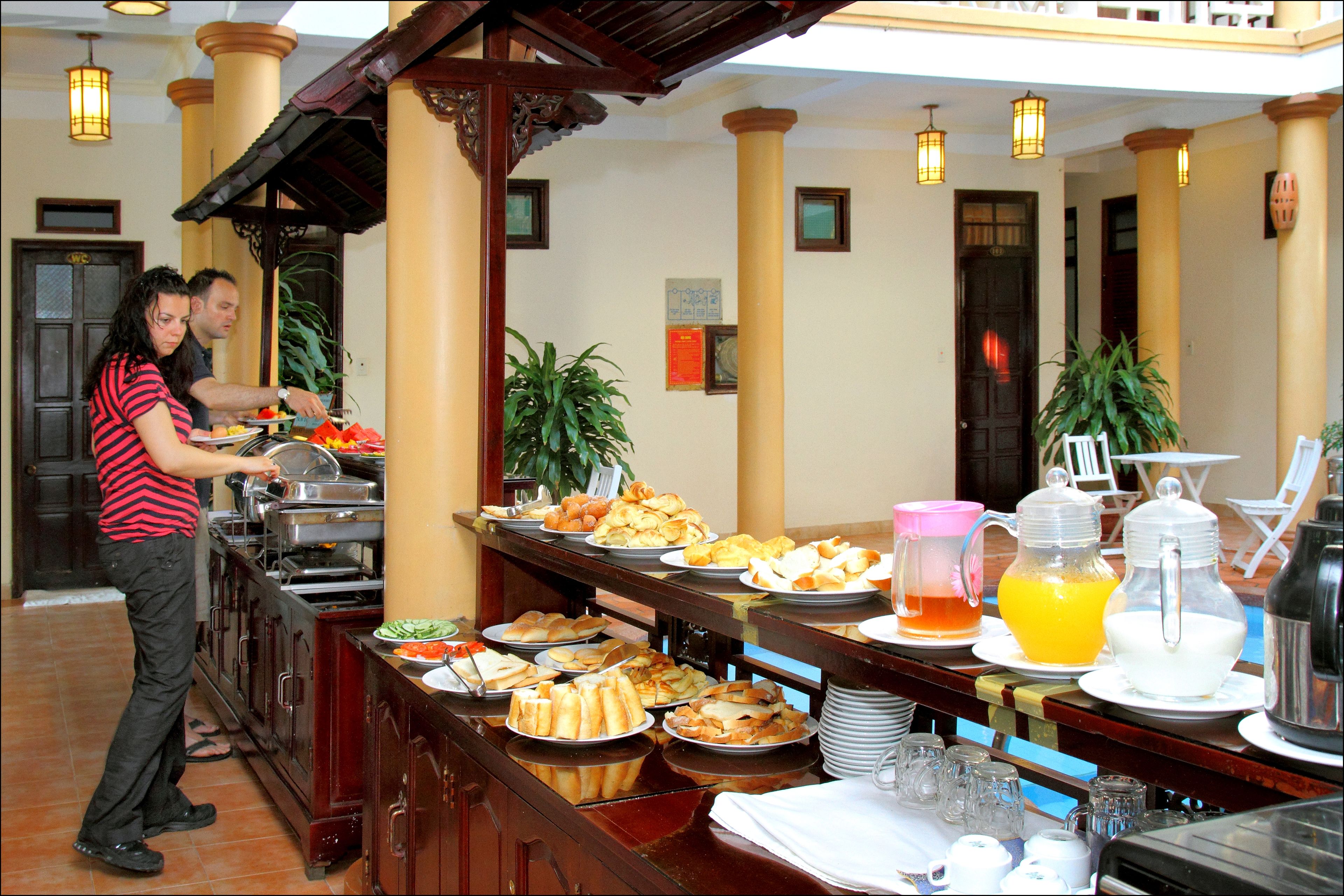 Un buffet proposant une variété de plats et de boissons, notamment des assiettes de nourriture, une carafe de jus d’orange et un distributeur d’eau.