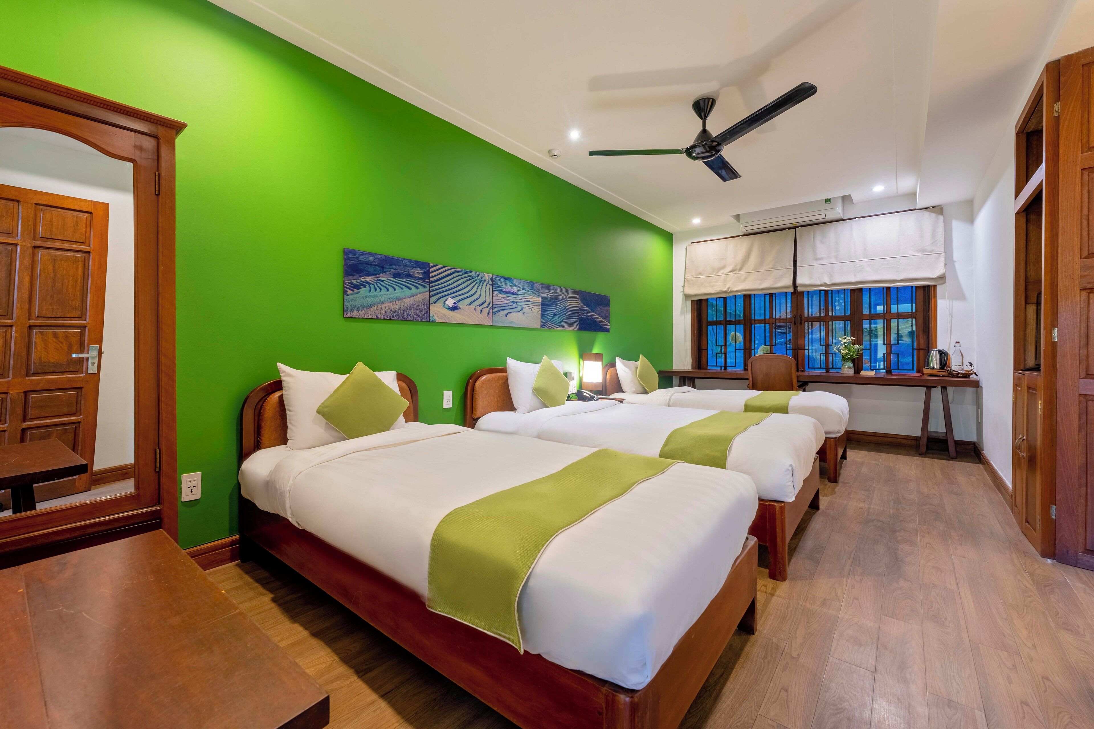 A hotel room with three beds, a desk, and a window with a view.