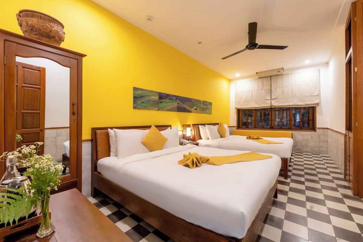 A hotel room with two beds, a checkered floor, a ceiling fan, and a large window with curtains.
