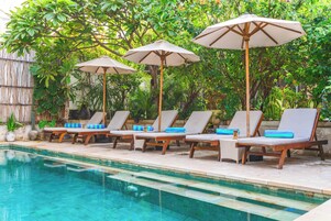 Área de piscina com espreguiçadeiras e guarda-sóis, rodeada por vegetação exuberante.