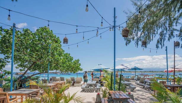 An outdoor seating area with tables and chairs, a beach view, and string lights. - Bale Sampan Bungalows (Gili Trawangan)