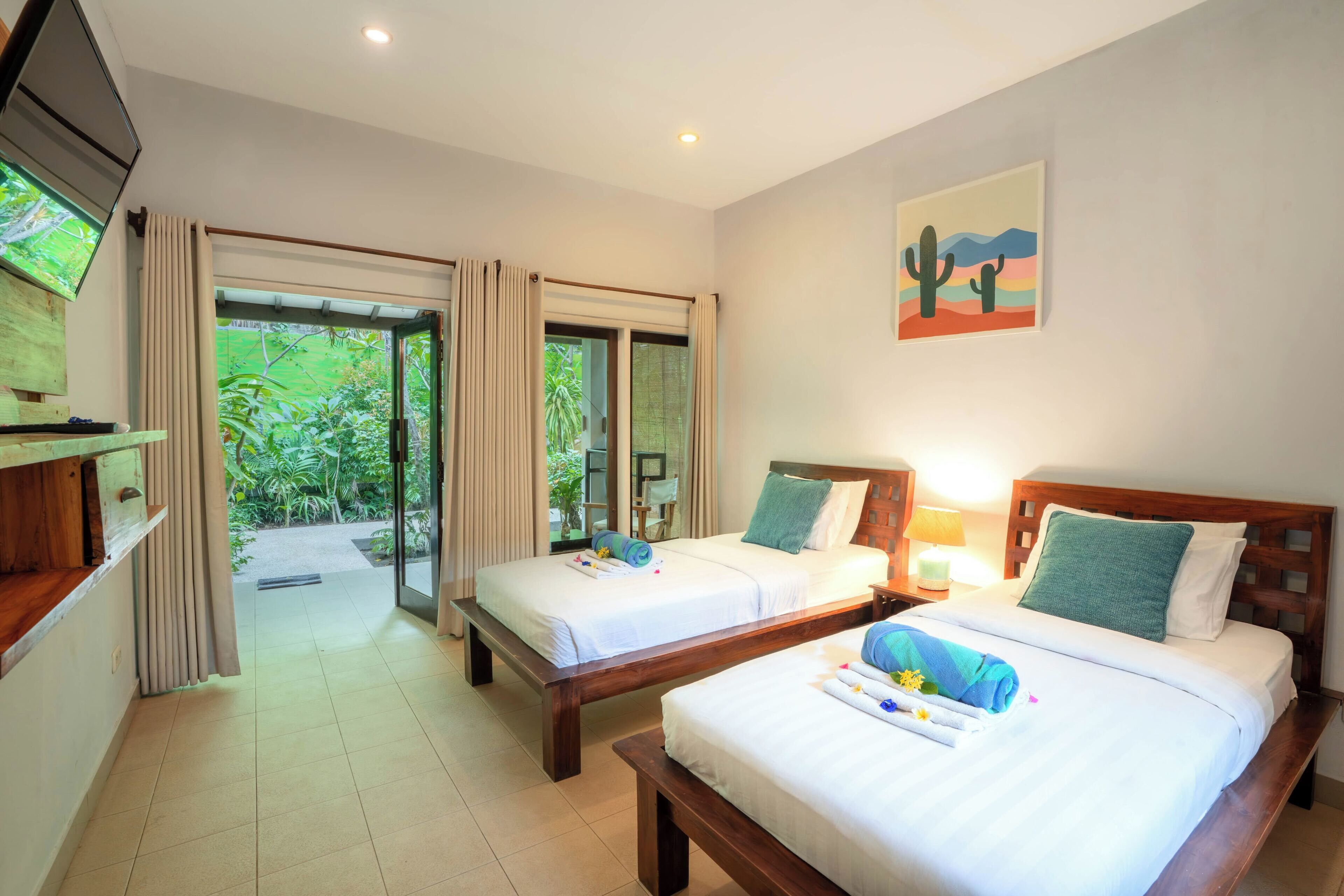A hotel room with two beds, a TV, a painting, and a view of greenery.