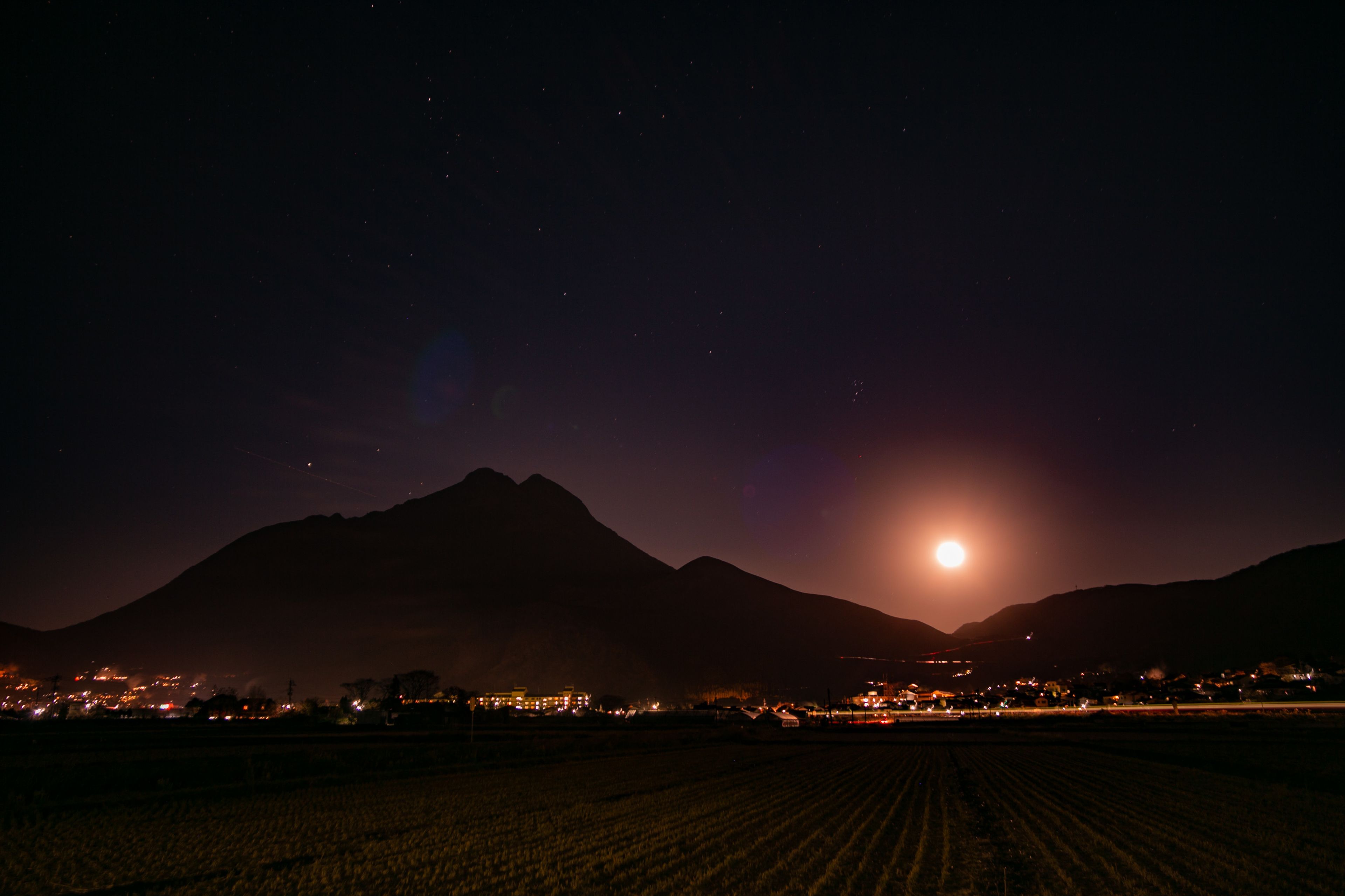 A nighttime landscape with a mountain in the background and a field in the foreground.