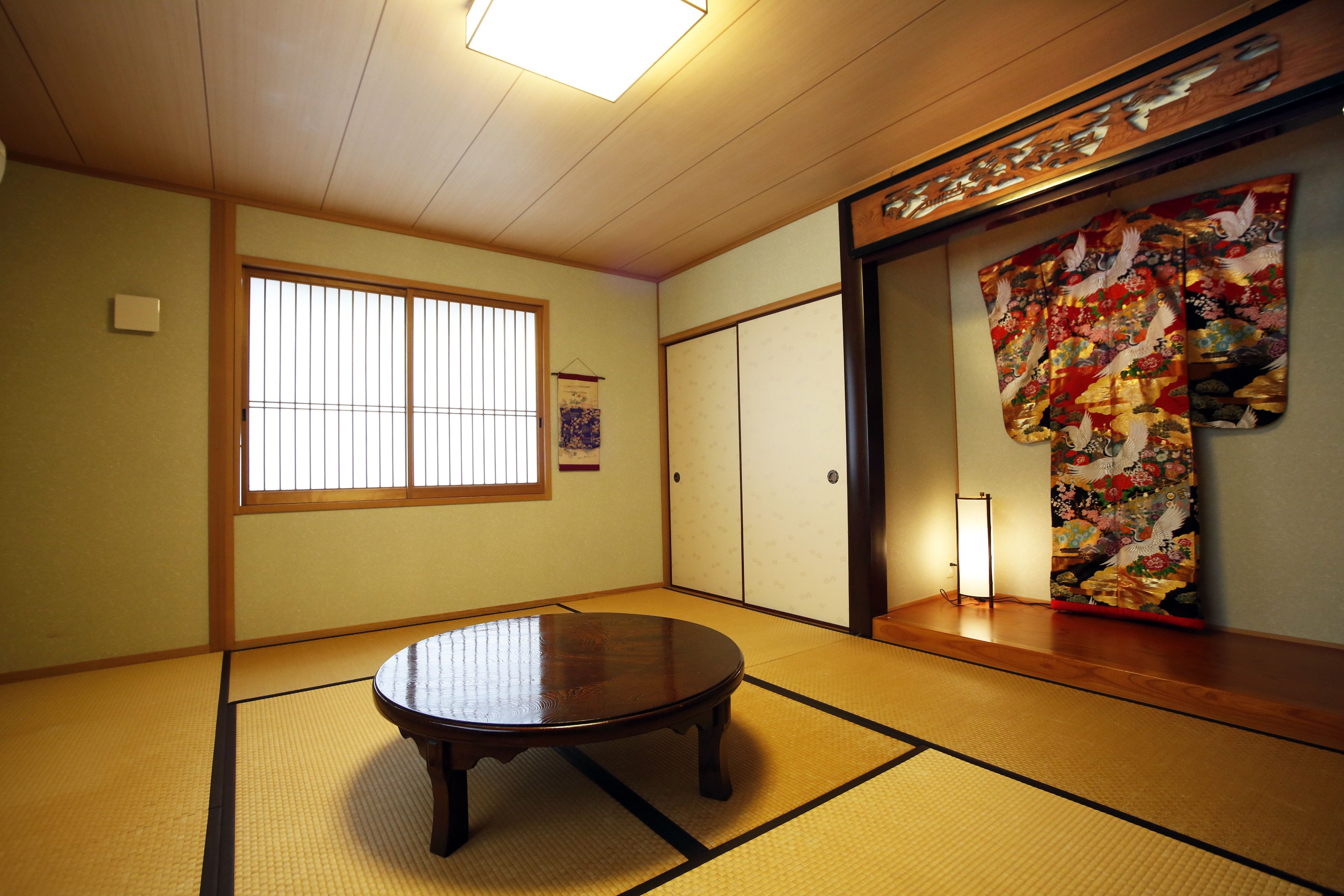 Een traditionele Japanse kamer met tatami vloerbedekking, een ronde tafel, schuifdeuren en een kleurrijke afbeelding aan de wand.