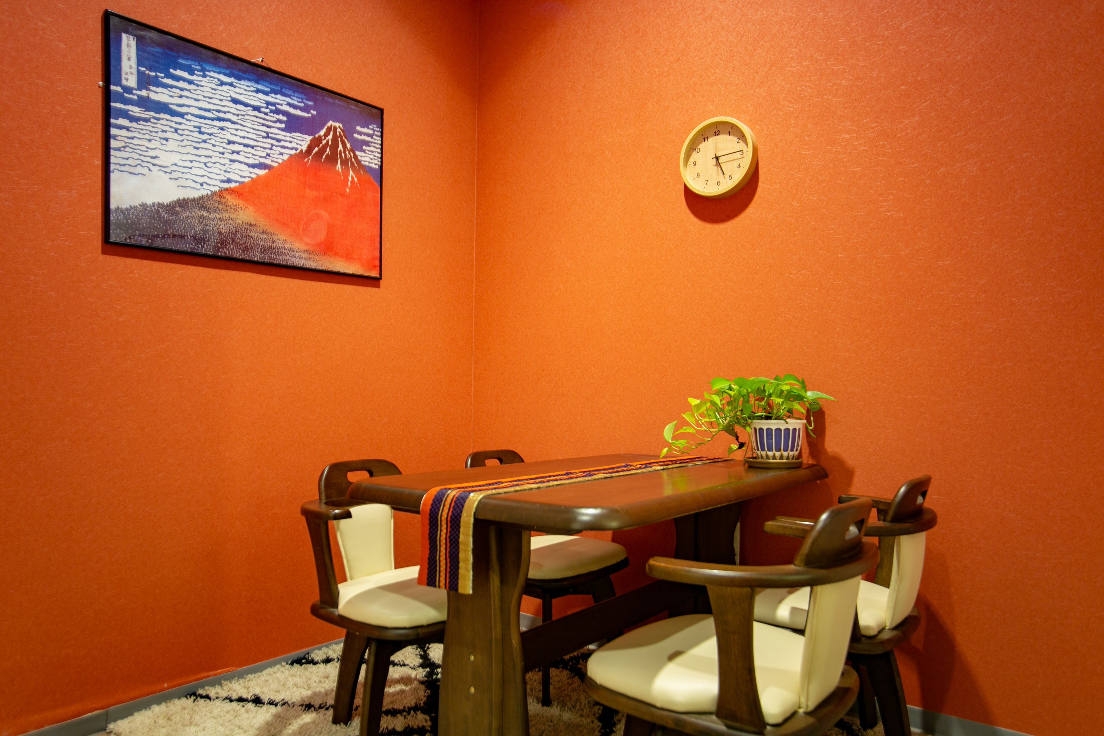 A conference room with a wooden table, six chairs, a clock, a framed picture of a mountain, and a potted plant.